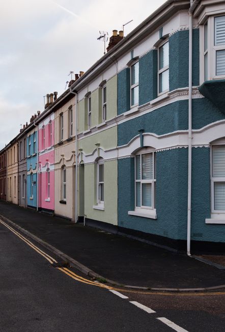 A row of terraced residential homes along Richmond Road KT1 with stone facades and curved bay windows. Each property features a distinct, colorful front door including dark green, purple, blue, and pi